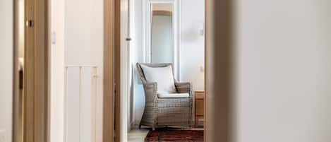 A hallway with a wicker chair, a wooden door, and a white wall.