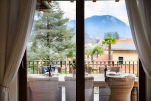 Un coin repas avec des chaises en osier et une table dressée pour deux personnes, offrant une vue sur un paysage montagneux.