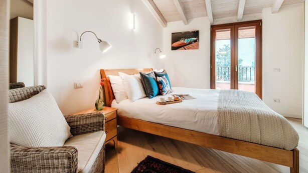 Ein Schlafzimmer mit einem hölzernen Bett, weißer Bettwäsche, einem Rattansofa, einem Nachttisch und einem Bild an der Wand.