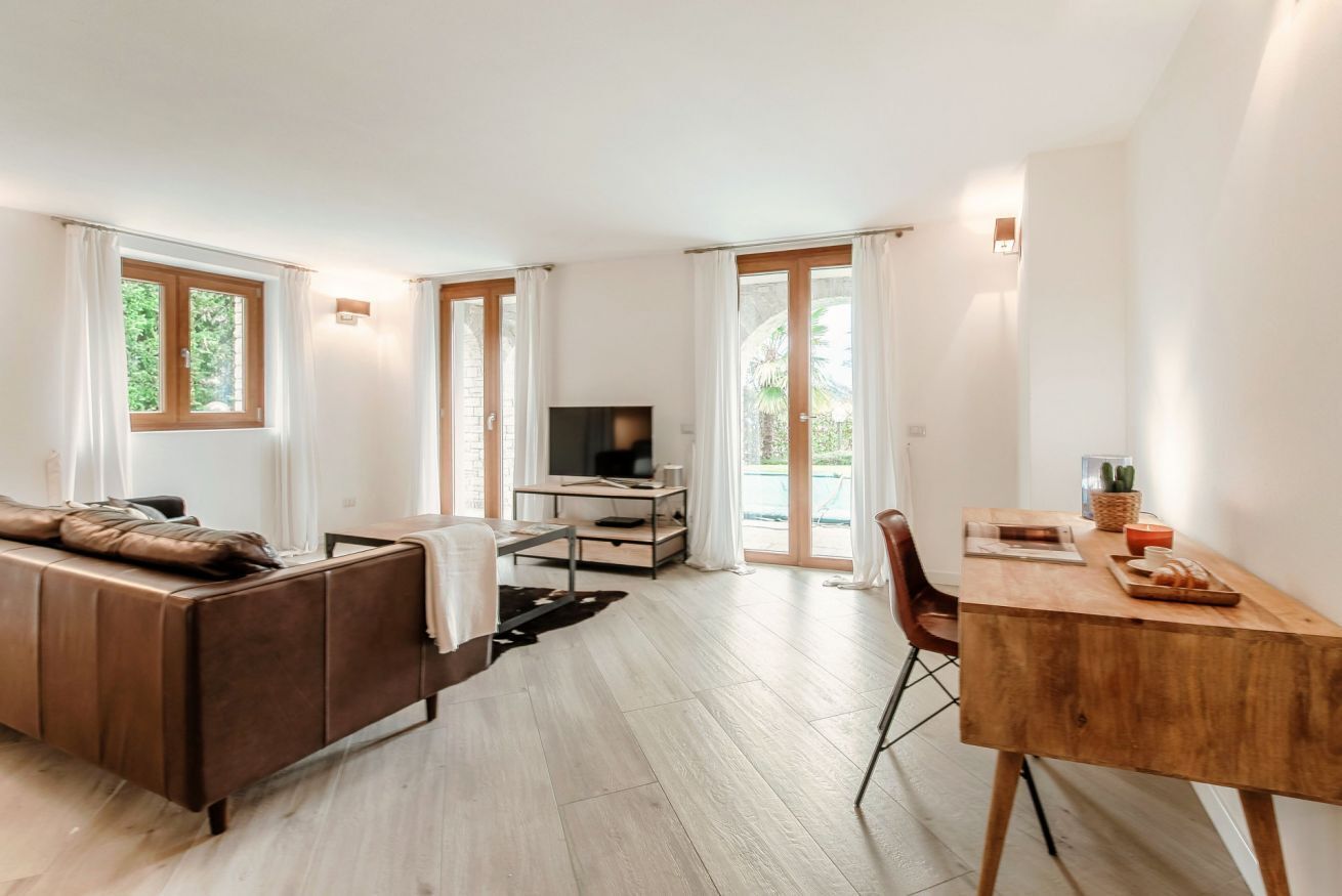 Un soggiorno moderno con divano, televisore, scrivania in legno e ampie finestre.
