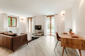 Ett modernt vardagsrum med en soffa, en tv, ett skrivbord i trä och stora fönster.