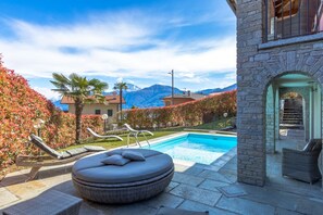 Ein Poolbereich mit Liegestühlen, einer Steinmauer und Blick auf die Berge.