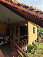 Una casa amarilla con una terraza de madera, una lavadora y una pequeña cocina.