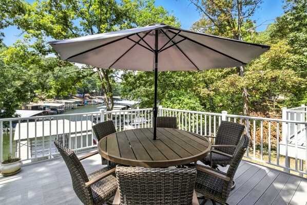 Une terrasse avec une table ronde et quatre chaises en osier, un parasol et une vue sur une rivière où naviguent des bateaux.