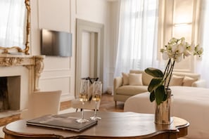 Een hotelkamer met een houten tafel, twee champagneglazen, een laptop, een bloemenvaas, een televisie en een bank.
