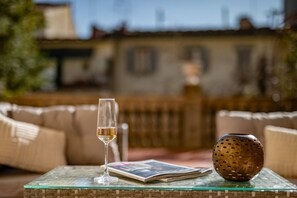 Una mesa de vidrio con una revista, una copa de vino blanco y un florero decorativo.