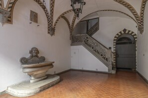 Un couloir agrémenté d’une fontaine, un escalier orné de rampes décoratives et une entrée fermée par un portail.