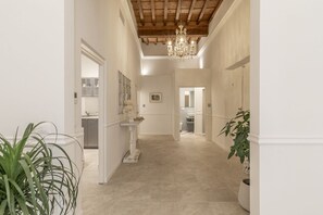 A hallway with a chandelier, a potted plant, and a view into a bathroom. - La casa di Liszt - Suite Madame Riblet (Firenze)