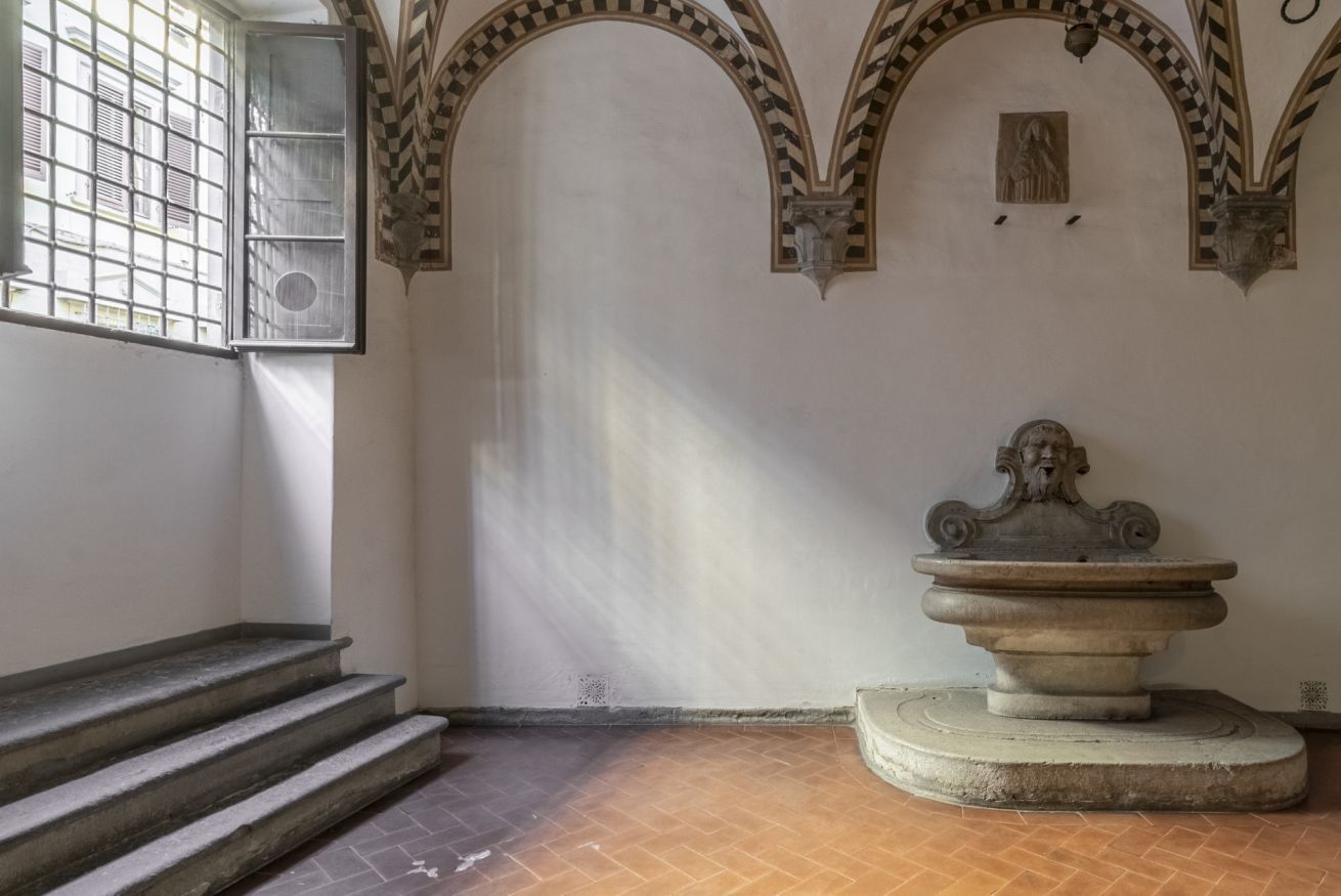A room with a stone fountain, a window with bars, and a staircase.
