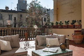 Ein sonniger Außenbereich mit Sitzgelegenheiten, einem schmiedeeisernen Gazebo, gepolsterten Sofas und einem Glastisch mit einem Weinglas und einem Buch.
