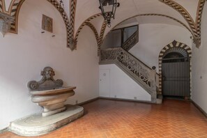 An interior with a stone fountain, a staircase with ornate railings, and a tiled floor.