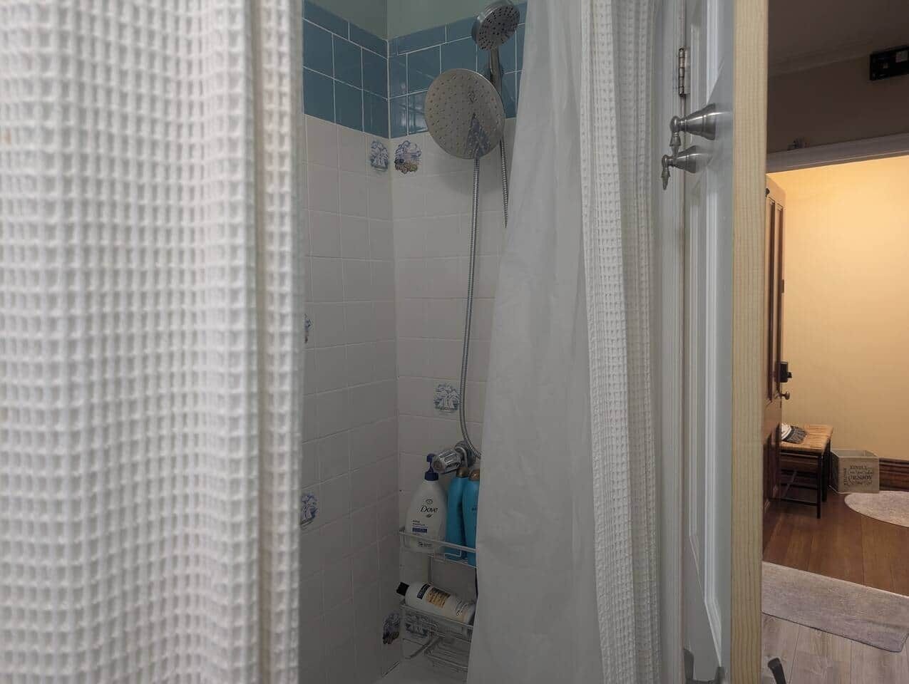 Ein Badezimmer mit Dusche, geflieste Wände und einer Tür zu einem anderen Raum.