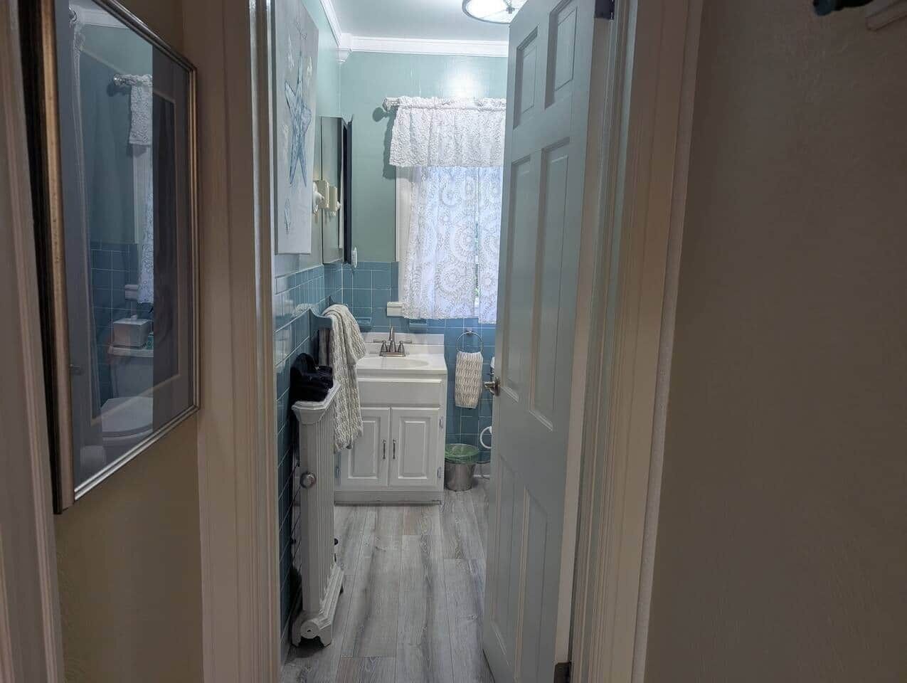 A narrow hallway leading to a bathroom with a sink, mirror, and towel rack.