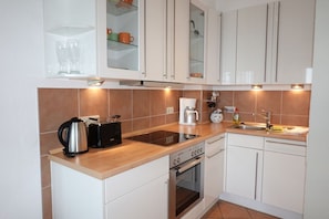 A modern kitchen with white cabinets, a stainless steel kettle, a coffee maker, and a built-in oven. - Welcome to Haus Bi de Wyk - your dream vacation awaits you! - Bi de Wyk (Wyk auf Föhr)
