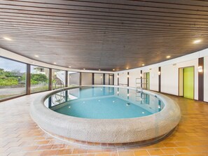 A modern indoor swimming pool with a curved design, surrounded by a tiled floor and walls, and equipped with a ladder for entry.