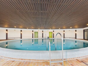 Ein Hallenbad mit Fliesenboden, Holzbalkendecke und einer Metallleiter.