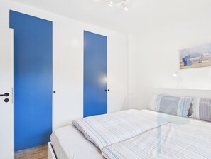 A bedroom with a bed, two doors, a painting on the wall, and a nightstand.