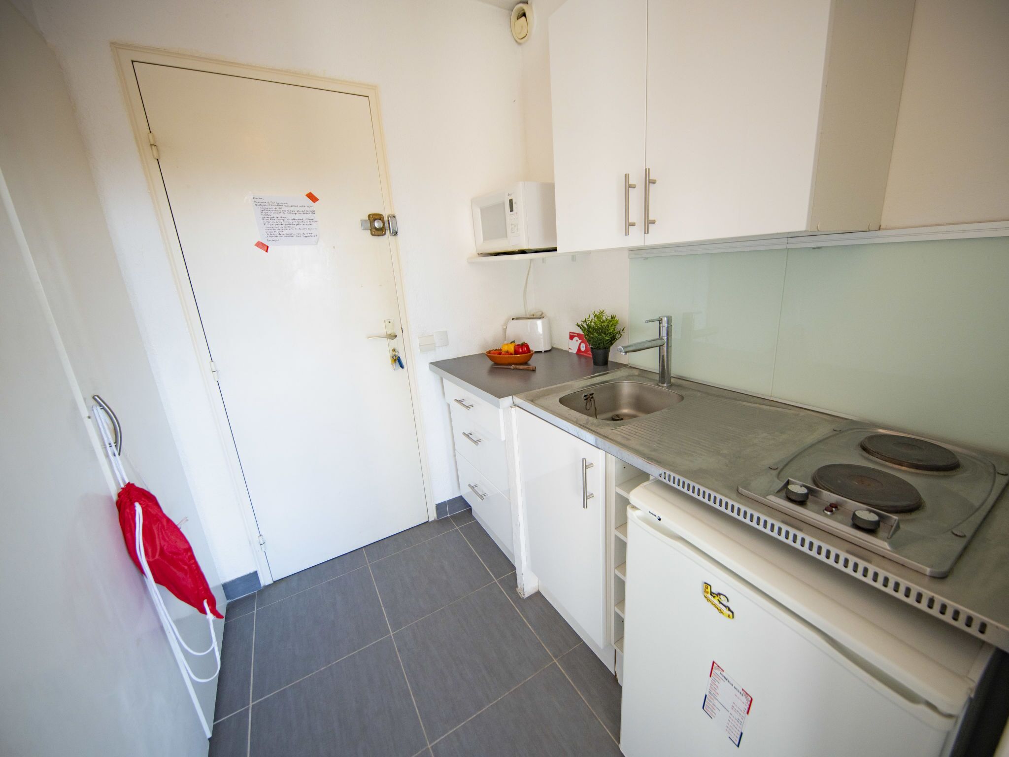 A compact kitchen with white cabinets, a stainless steel sink, a built-in stove, and a small refrigerator.