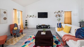 Una sala de estar moderna con sofá, sillón, mesa de centro y televisor en la pared.