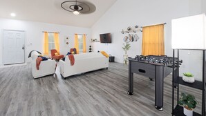 Una sala de estar moderna con un conjunto de sofás, una mesa de fútbol de mesa y un televisor montado en la pared.