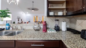 Una cocina con encimeras de granito, un fregadero, una cafetera, una licuadora y un armario con estantes.