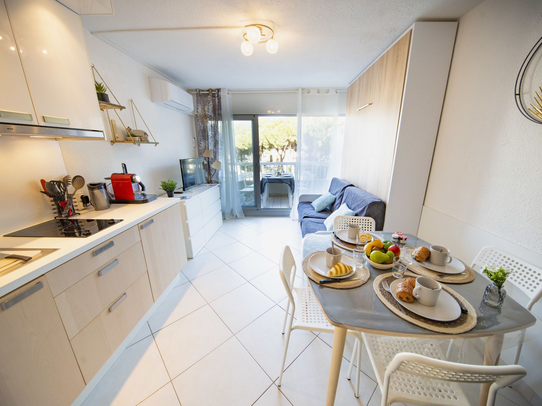 A modern kitchen with white cabinets, a dining table set with plates, cups, and a fruit bowl.