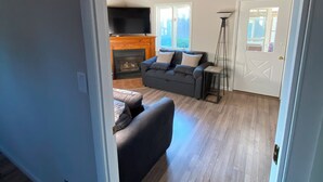 Una sala de estar con chimenea, un sofá, un televisor y una lámpara de pie.