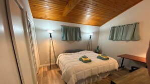 Un dormitorio con techo de madera, una cama con edredón blanco, dos lámparas de pie y una mesita.