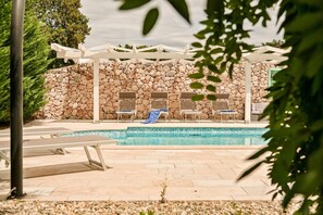 Een zwembadgedeelte met stenen muren, ligbedden en een pergola.