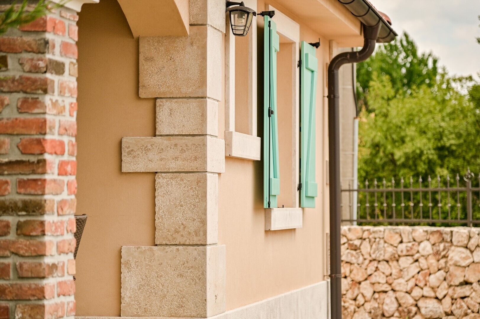 A corner of a building with a brick wall, a stone wall, and a metal fence.