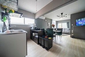 A modern kitchen with a built-in island, a dining area with a table and chairs, and a living room with a sofa and a TV. - VITA (Furano)