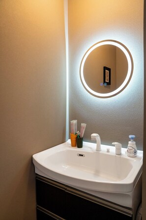 A bathroom with a white sink, a round mirror with a light, and toiletries. - VITA (Furano)