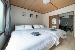 A double bed with white bedding, a grey towel, and a wooden ceiling. There are three framed pictures on the wall and a mirror on the door. - VITA (Furano)