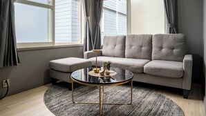 A living room with a grey sofa, a round glass coffee table, and a grey rug. - VITA (Furano)