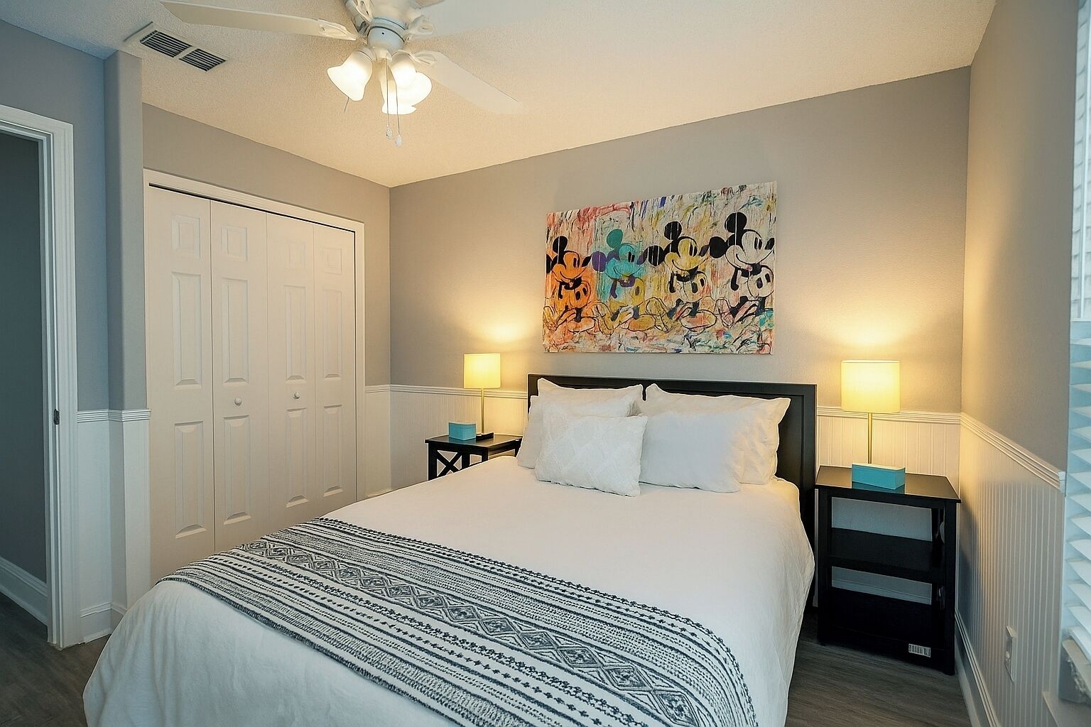 Une chambre à coucher avec un grand lit, deux tables de chevet, un ventilateur de plafond et un tableau mural.