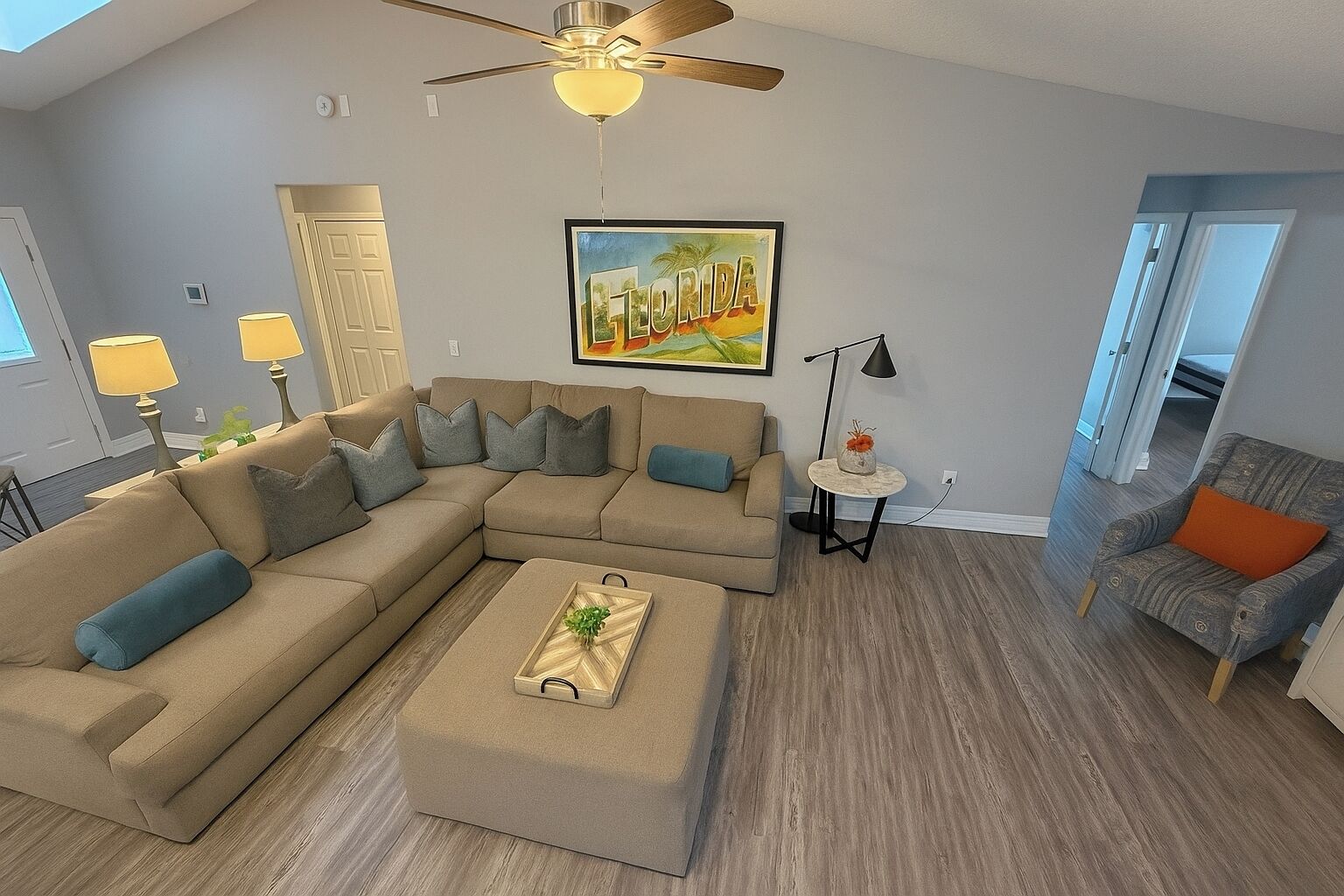 A modern living room with a sectional sofa, a coffee table, a floor lamp, and a painting of Florida.