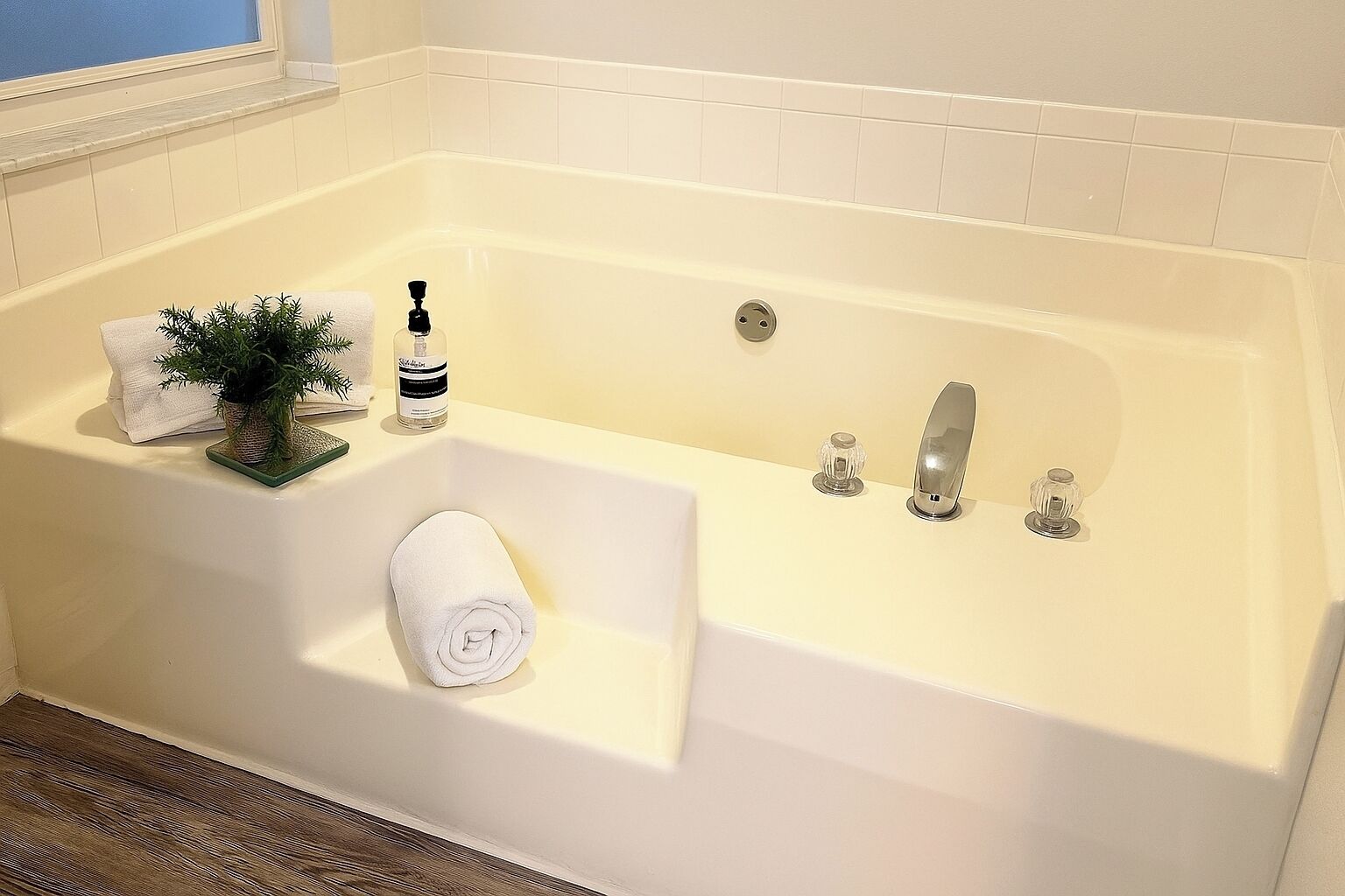 A bathroom with a bathtub, a towel, a bottle of soap, and a small plant.