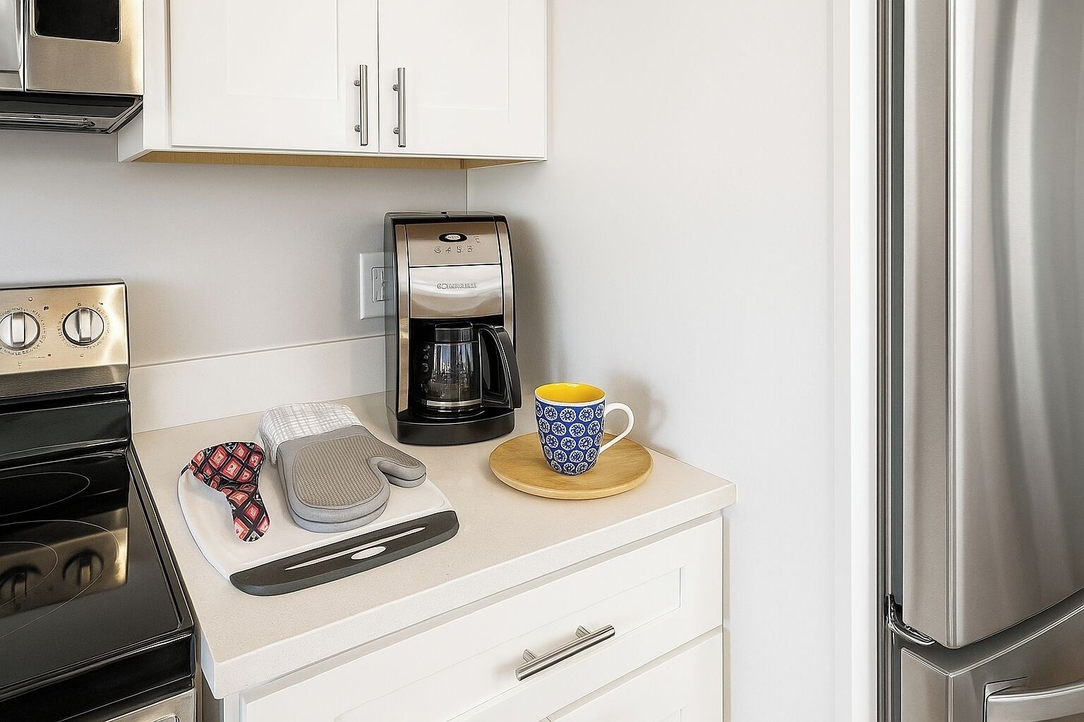Una cocina con cafetera, taza, tabla de cortar y dos guantes de horno.