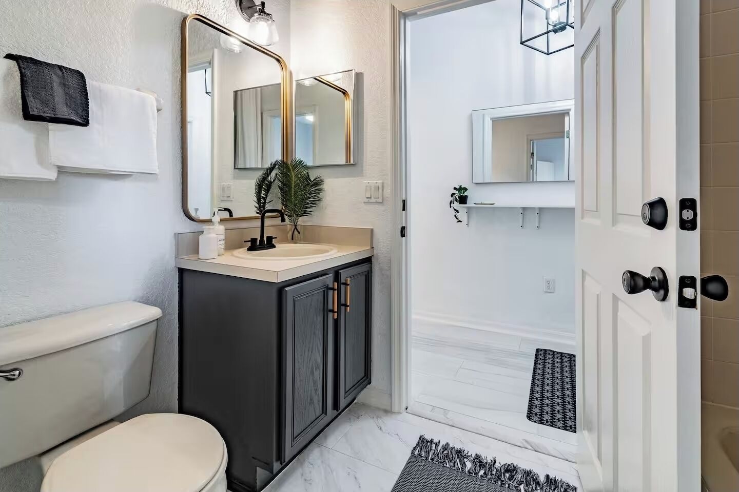 A modern bathroom with a toilet, sink, and mirror, featuring a black cabinet and a small plant.