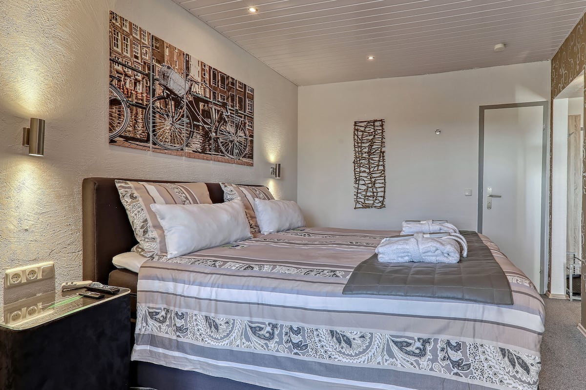 A hotel room with a large bed, a wall-mounted TV, and a painting of bicycles.