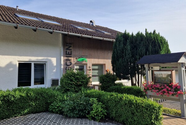 A building with a tiled roof, a green awning, and a signboard. - Suit & Frühstück zum Latschen  (Mauth)