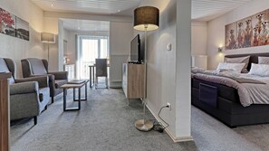 A modern hotel room with a sofa, a small table, a TV, and a bed with a patterned bedspread. - Suit & Frühstück zum Latschen  (Mauth)