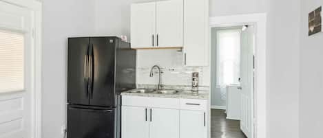 Una cocina compacta con armarios blancos, un refrigerador negro y un lavamanos de acero inoxidable.