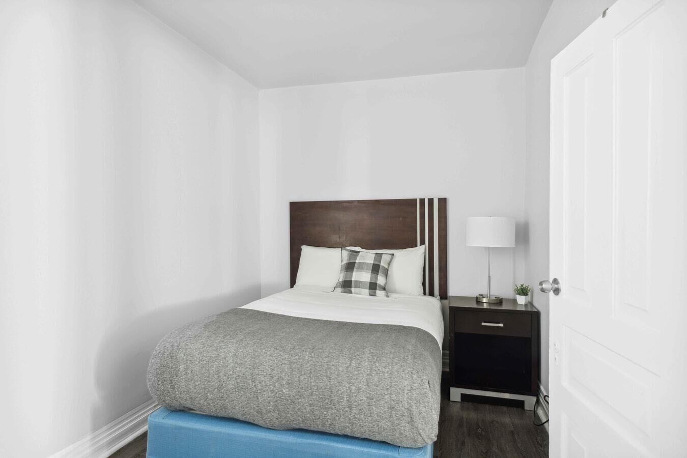 A neatly arranged bedroom with a bed, bedside table, lamp, and a door.