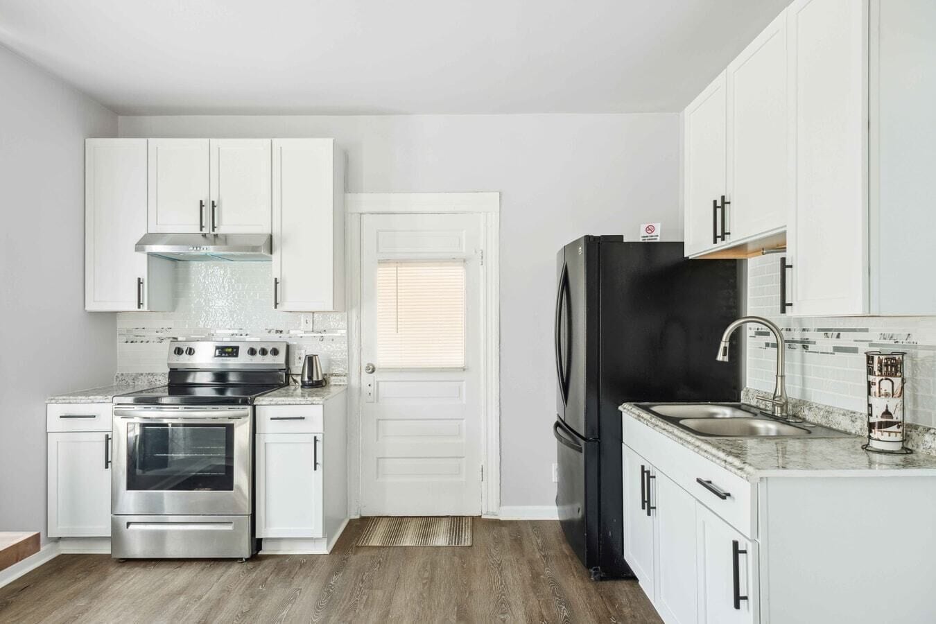 A compact kitchen with white cabinets, stainless steel appliances, and a black refrigerator.