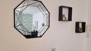 Une pièce avec un miroir aux formes géométriques, une petite étagère ornée d’objets décoratifs et un téléphone fixé au mur.