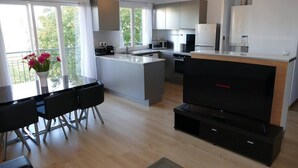 A modern kitchen with a central island, a dining area with a table and chairs, and a flat-screen TV on a stand.