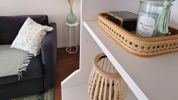 A modern living room with a dark sofa, a small side table with a vase of pampas grass, and a shelf with decorative items. - Gd 4P 85m² hyper centre Disney (Chessy)
