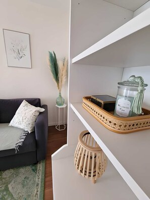 A modern living room with a dark sofa, a small side table with a vase of pampas grass, and a shelf with decorative items.