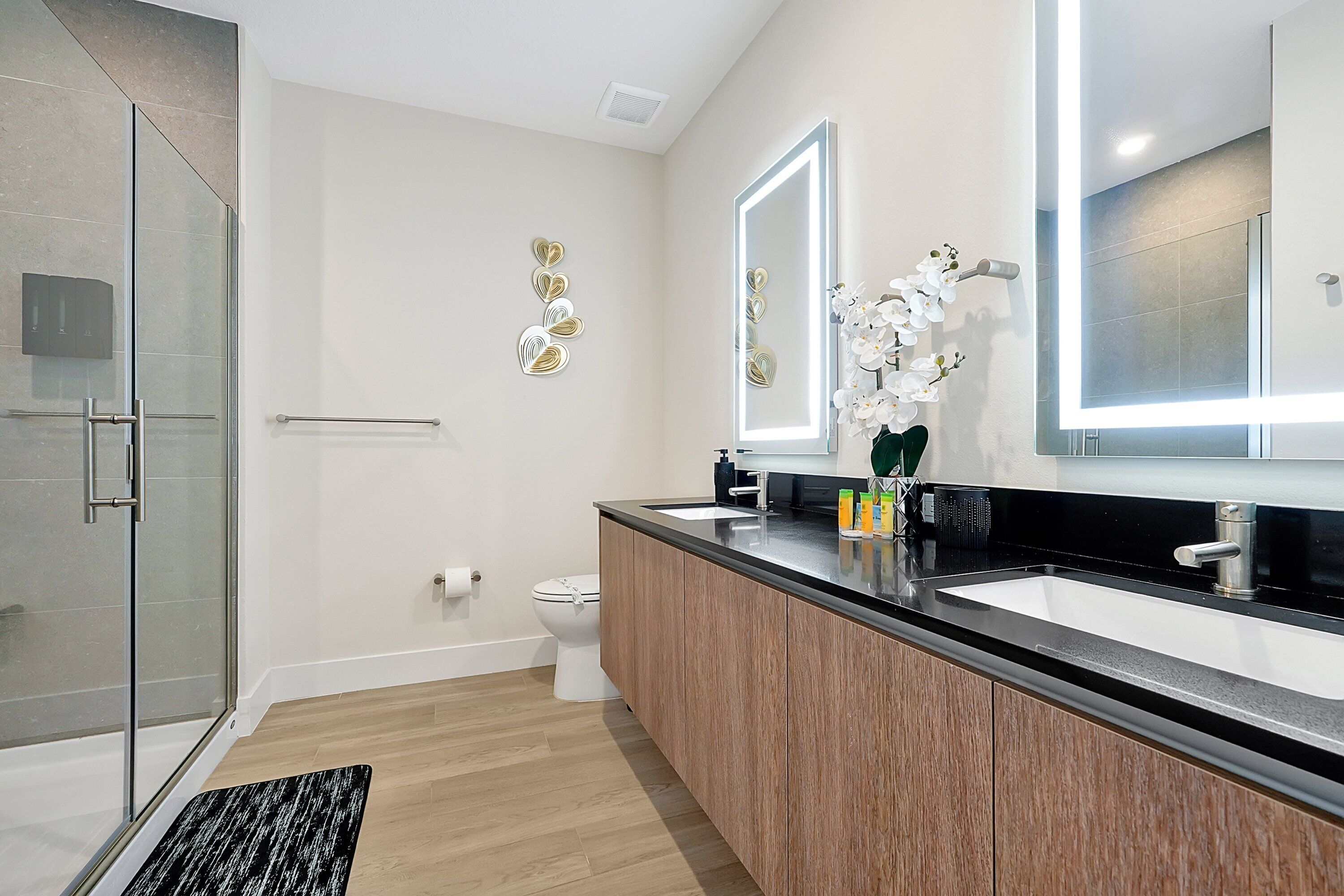 Un baño moderno con cabina de ducha de vidrio, tocador de madera y un espejo grande con iluminación integrada.